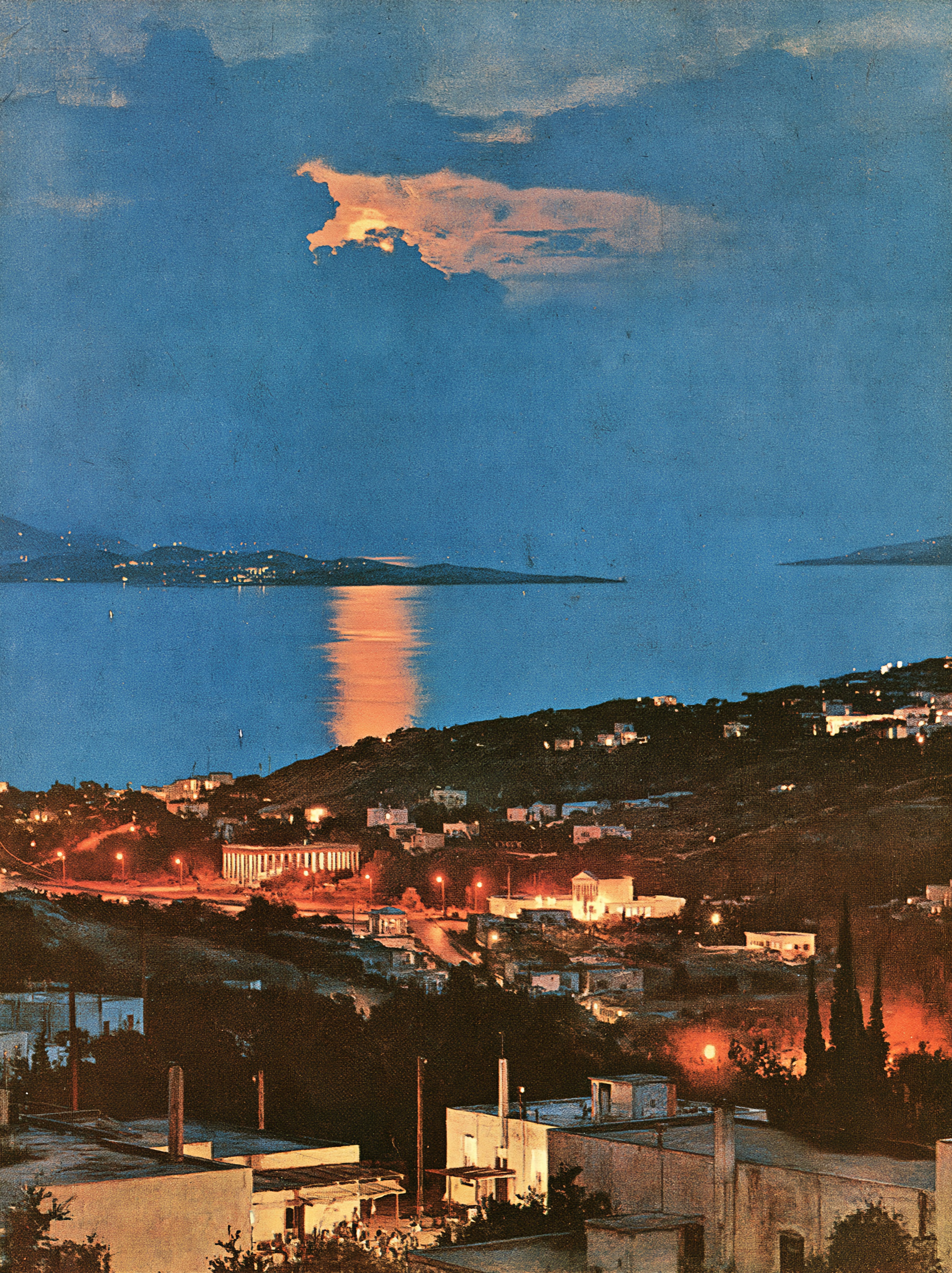 Moonlight breaking through blue clouds and reflecting across the sea above a coastal town at night.