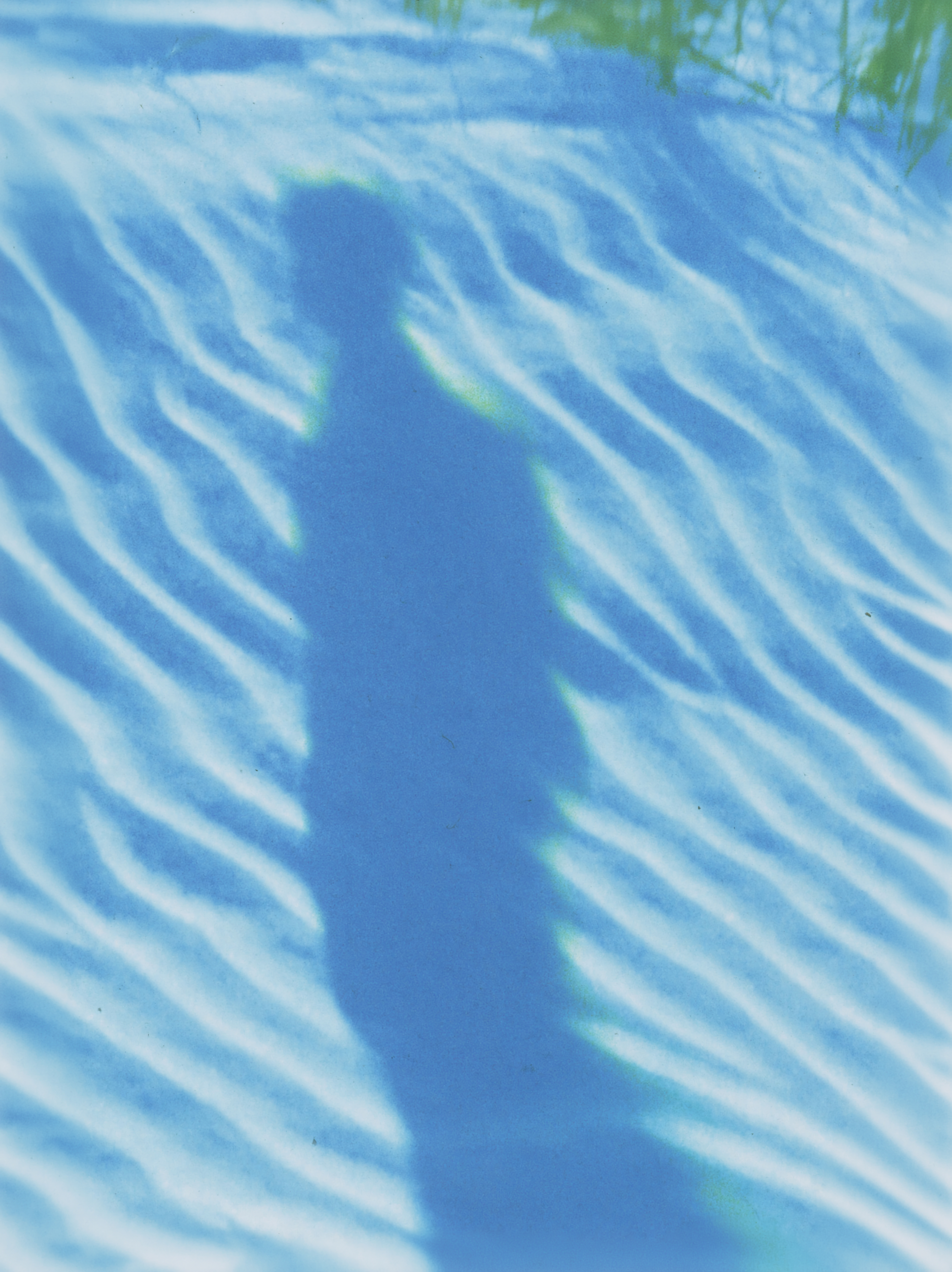 A figure’s shadow amid blue water and rippling bands of light.
